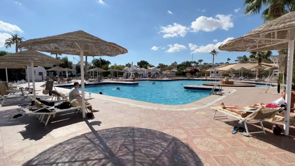 La piscina vicino alla piazzetta centrale del Domina Coral Bay, con ombrelloni di paglia e vista sul complesso