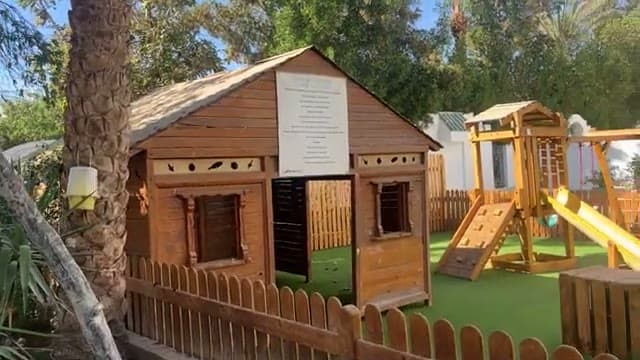 La casetta in legno del parco giochi del Falcon Hills, con scivolo e prato sintetico, accanto alla piscina
