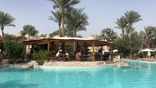 La piscina centrale di The Grand Hotel con il bar in legno raggiungibile dall'acqua e le palme intorno