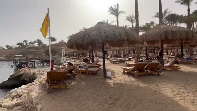 La spiaggia di The Grand Hotel con gli ombrelloni in paglia ravvicinati, i lettini in legno e il pontile sulla sinistra