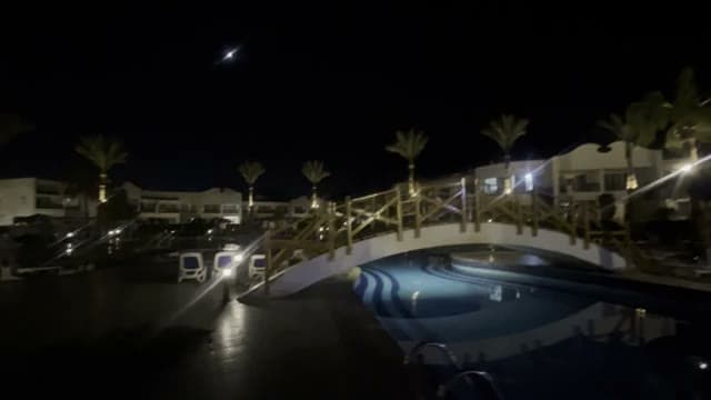 La piscina del Panorama Naama Heights illuminata la sera con il ponte di legno e le palme