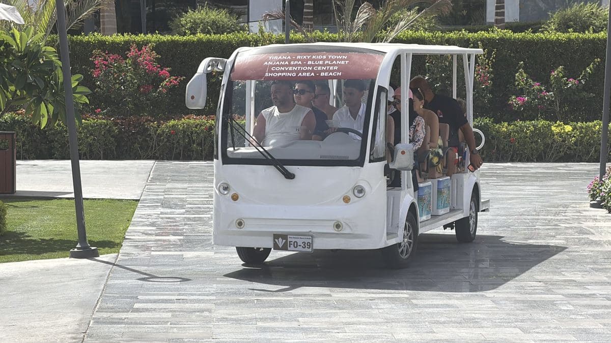 Una delle navette elettriche bianche del Rixos Radamis con gli ospiti a bordo, sul vialetto tra le siepi