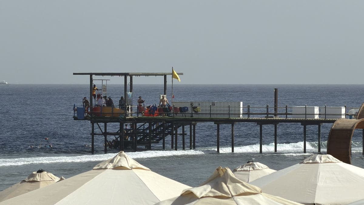 Il pontile del Rixos Radamis con la piattaforma coperta in fondo, visto dalla spiaggia tra gli ombrelloni
