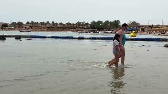 Una mamma e una bambina camminano nell'acqua che arriva alle ginocchia vicino alla linea delle boe al Sinbad Beach