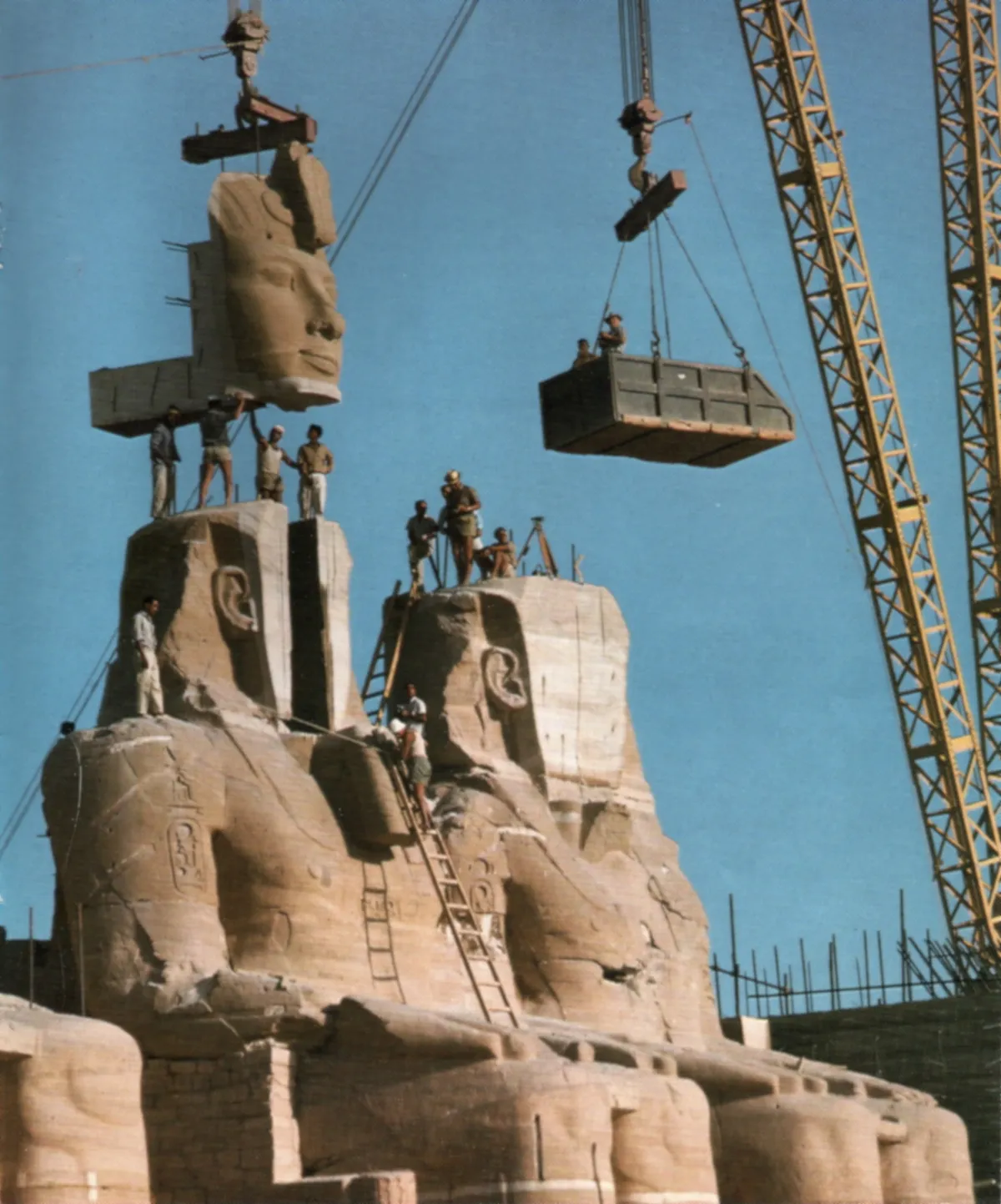 Cantiere di Abu Simbel nel 1966: la gru solleva il volto tagliato di un colosso di Ramses II mentre gli operai lavorano sulle spalle della statua