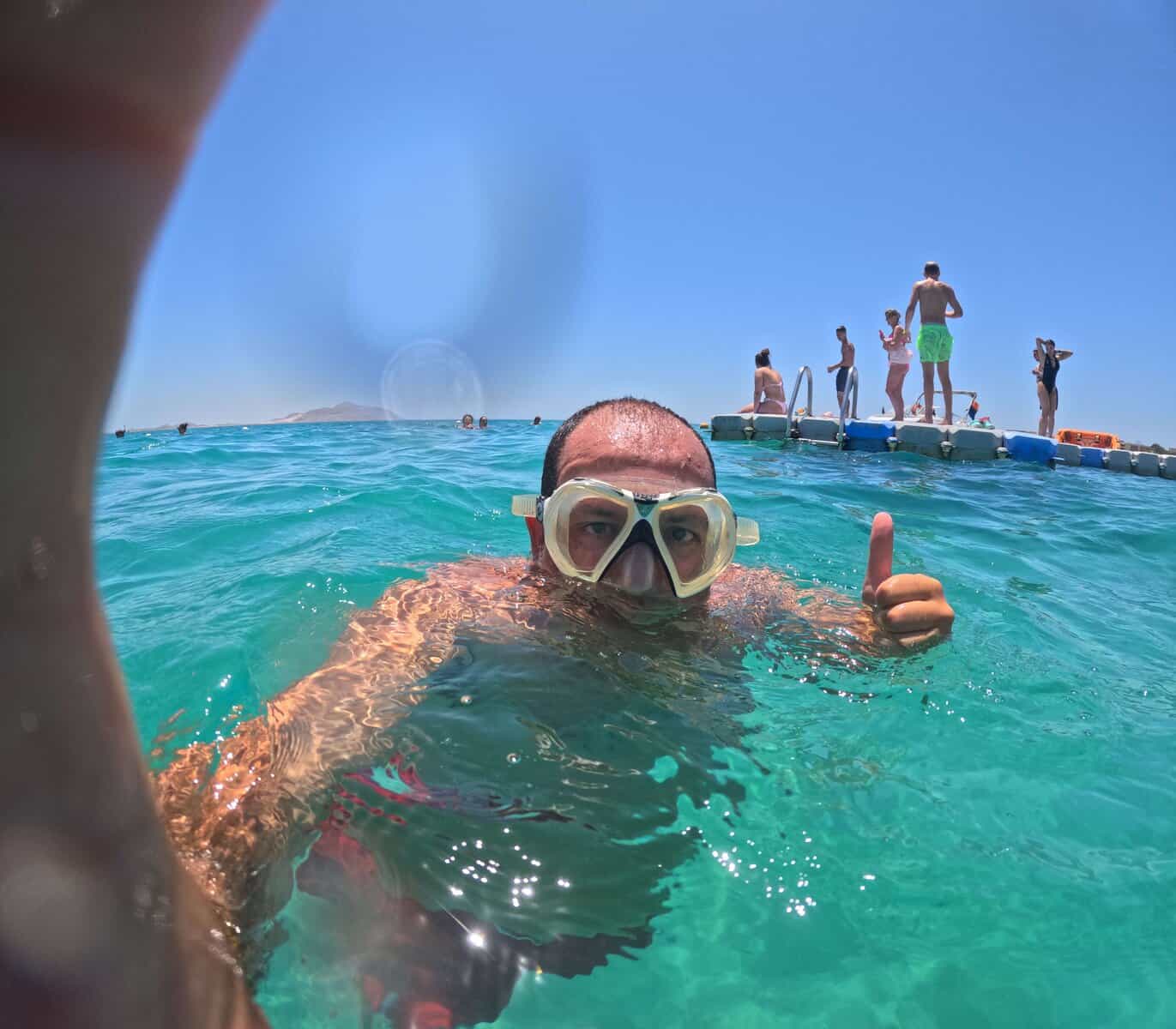 Snorkeling d'estate a Sharm: un bagnante con la maschera fa il segno ok nell'acqua turchese, dietro una piattaforma galleggiante con altre persone