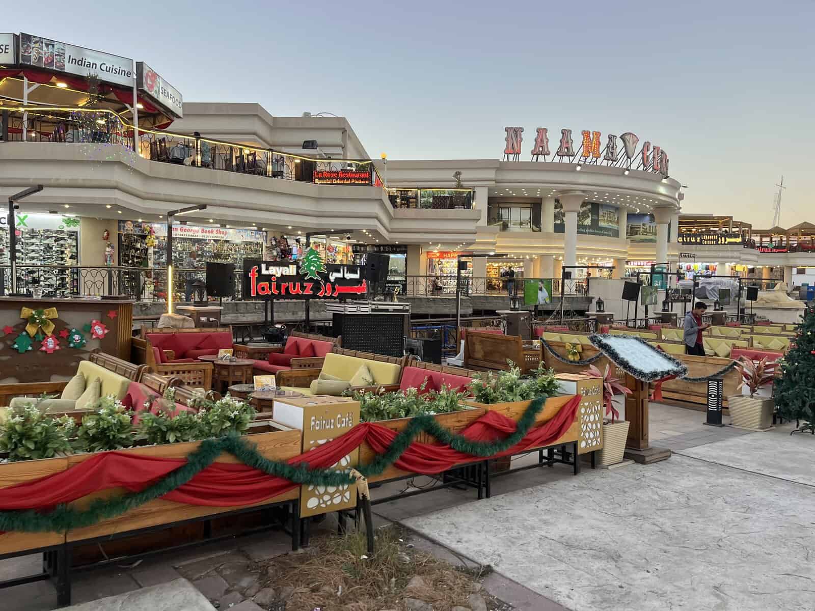 Centro commerciale moderno con insegne in arabo e inglese, decorazioni natalizie rosse e verdi, negozi e caffè a livello strada