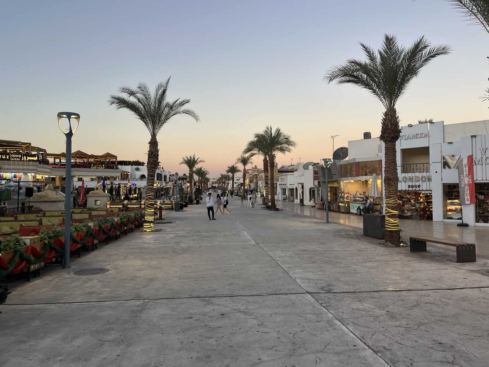La passeggiata di Naama Bay a dicembre all'ora del tramonto: palme illuminate, addobbi di Natale sui tavolini dei locali e gente che passeggia in maglietta