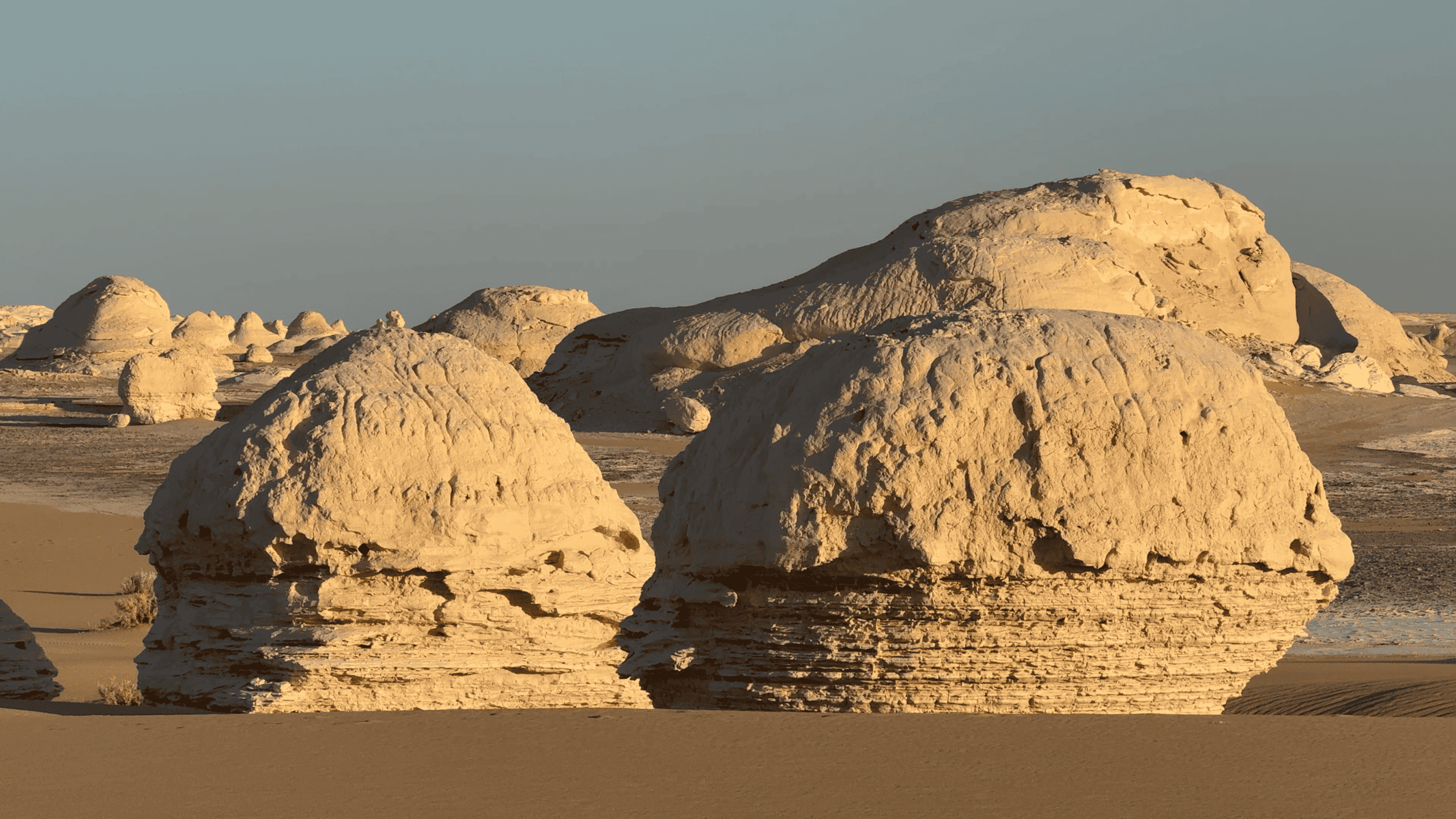 Formazioni rocciose bianche e beige nel deserto bianco egiziano con dune di sabbia sullo sfondo al tramonto