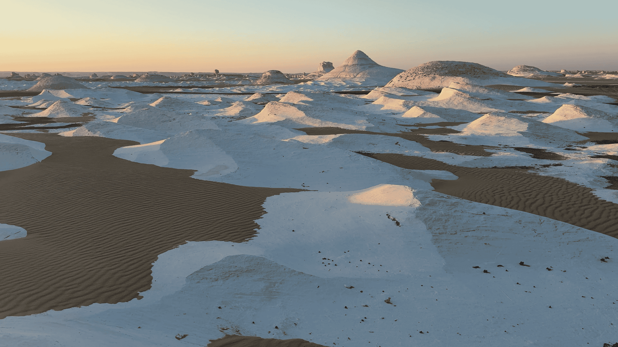 Paesaggio desertico bianco con formazioni rocciose coniche al tramonto, pozze d'acqua e sabbie ondulate al White Desert in Egitto