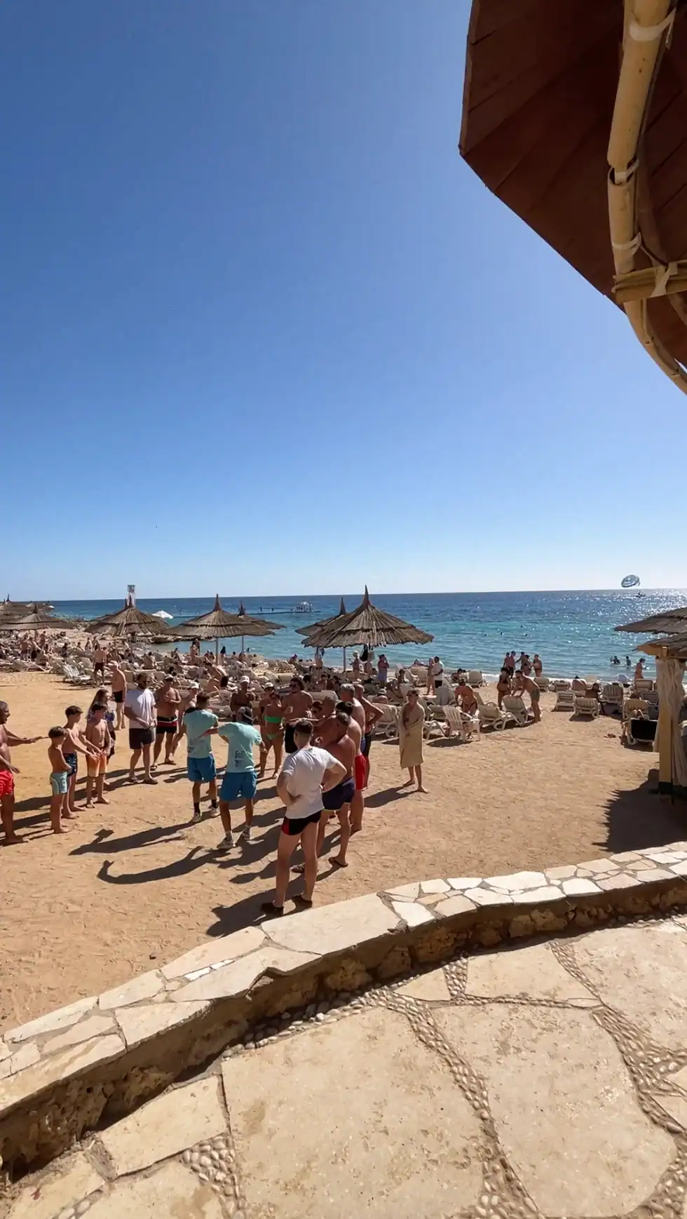 Spiaggia affollata di turisti con ombrelloni in paglia, mare cristallino e cielo sereno in una località balneare egiziana