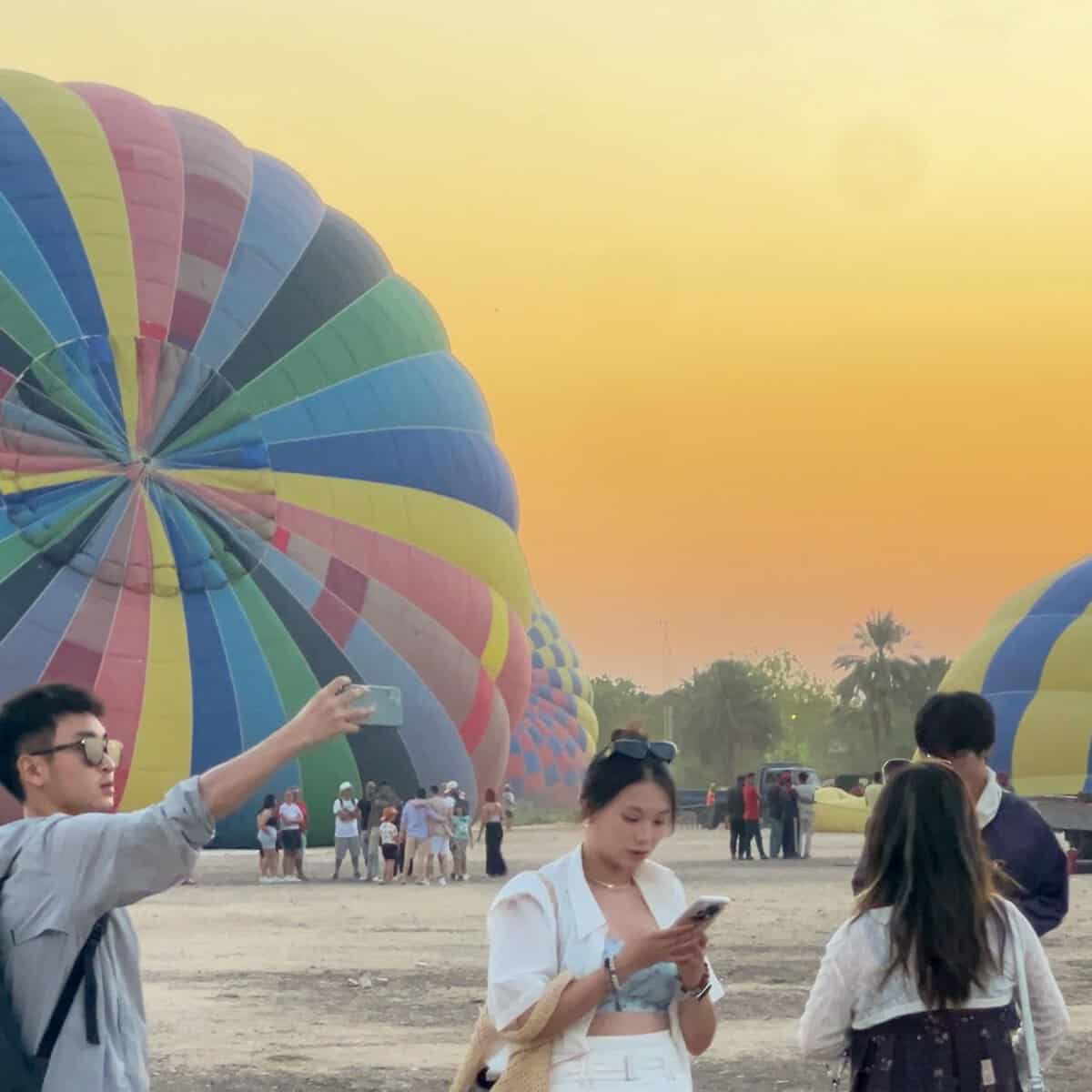 Persone ammirano palloni aerostatici colorati al tramonto in Egitto, con palme sullo sfondo
