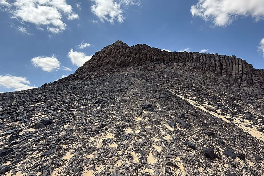 Formazione rocciosa vulcanica con colonne di basalto esagonale su pendio desertico sotto cielo blu