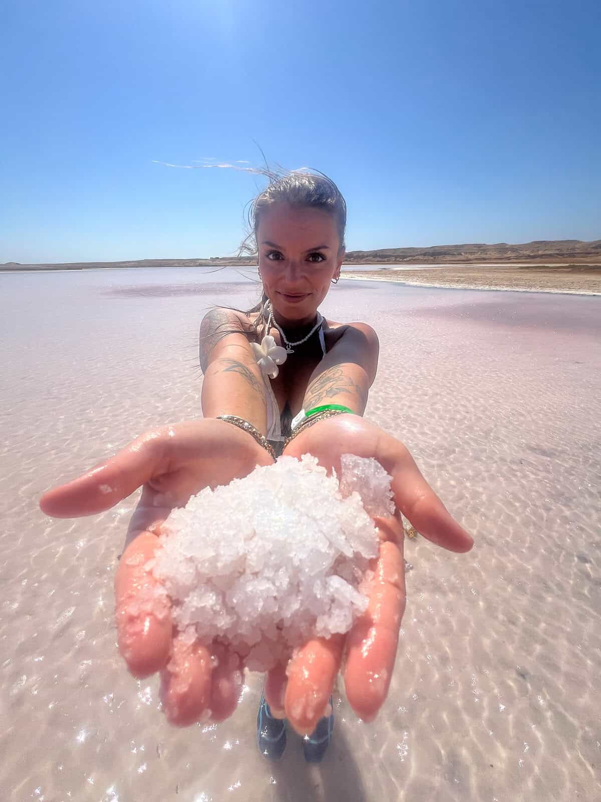 Donna sorride mostrando cristalli di sale nelle mani in una laguna salata rosa deserto