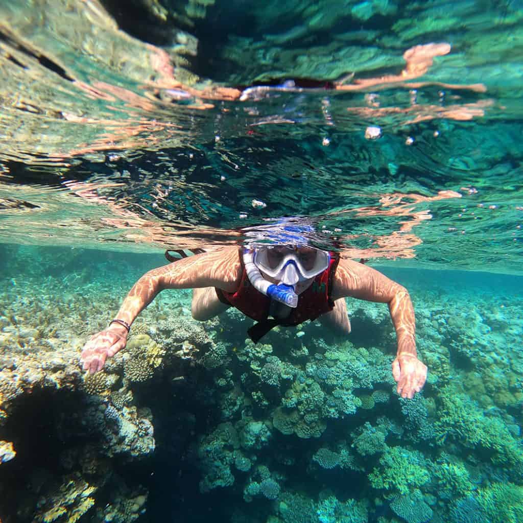 persona con maschera e boccaglio fa snorkeling nel mar rosso con la barriera corallina sullo sfondo