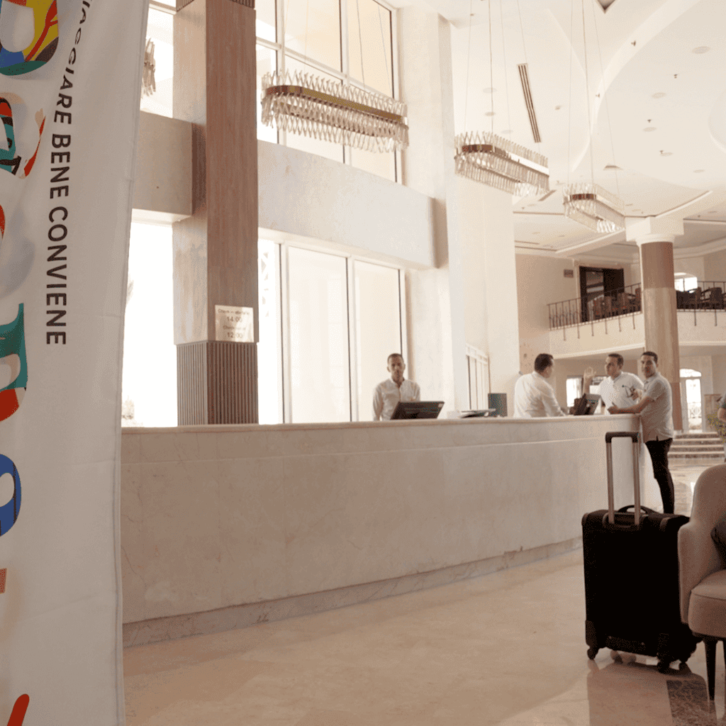 lobby bianca con finestre ampie da cui entra luce naturale, valigie , receptionisti e bandiera con logo di baobab all' ivy cyrene sharm