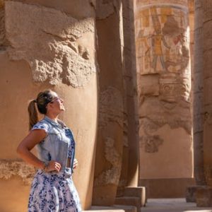 Woman in Luxor Temple admiring ancient carved columns in sunlight.