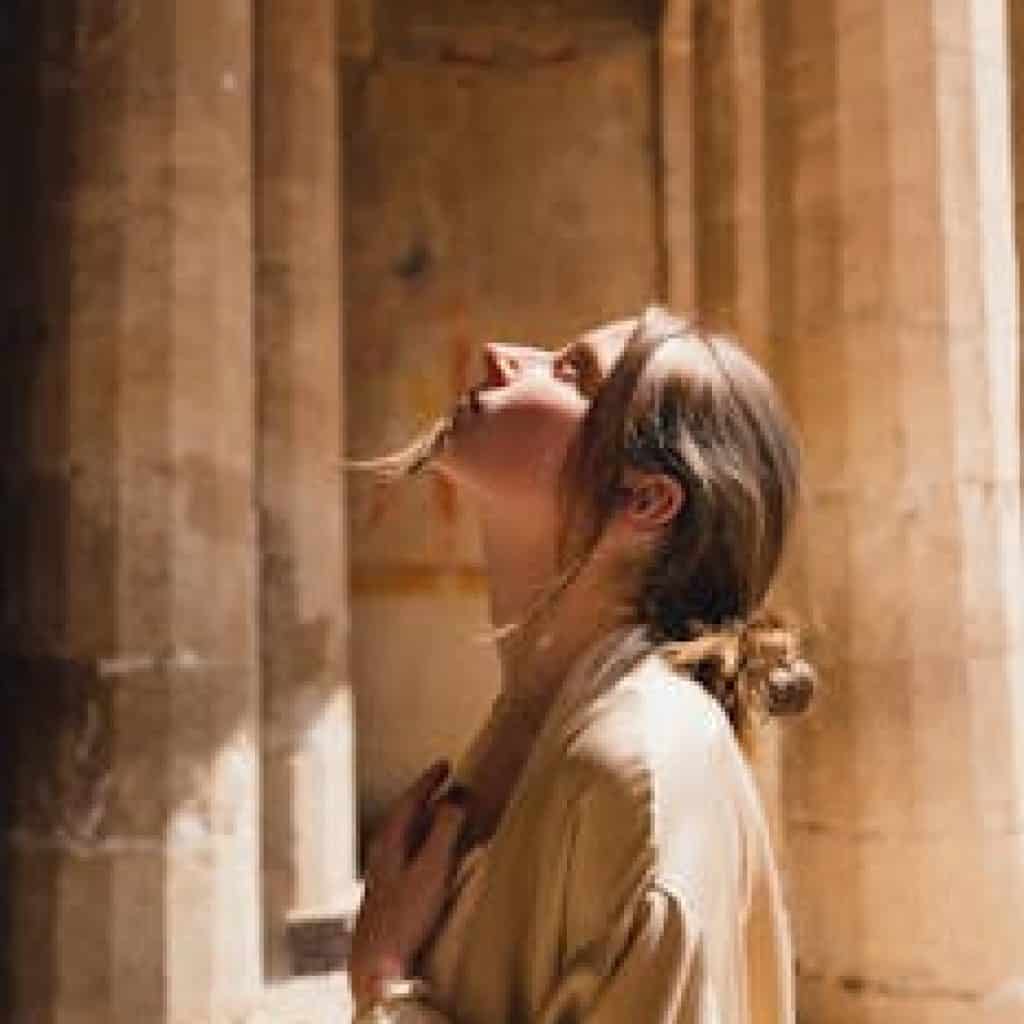 A woman in a beige coat looks up inside ancient Egyptian temple ruins.